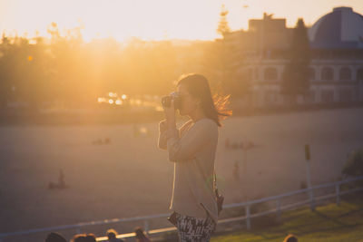 Woman photographing in park during sunset