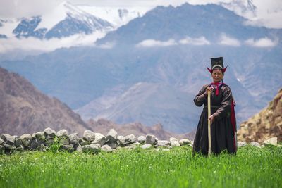 Portrait of mature woman standing on grassy field against mountains