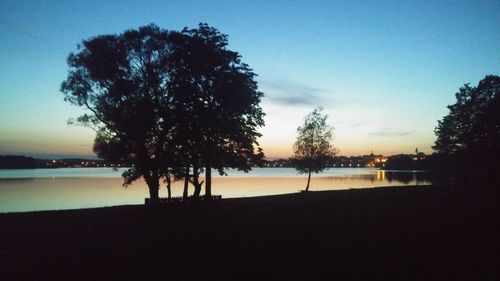 Silhouette trees by lake against sky at sunset