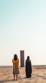 Rear view of women standing on field against sky