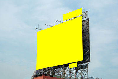 Low angle view of yellow sign on pole against sky