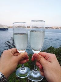 Cropped hands of man holding champagne flute against lake