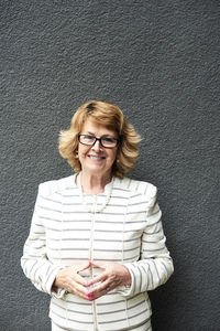 Portrait of smiling senior businesswoman against grey wall