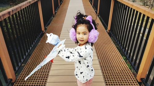 Portrait of cute girl with kite standing on footbridge