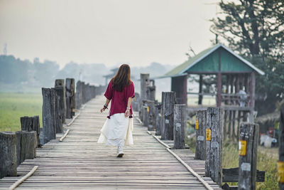 Full length of woman walking on footbridge against sky
