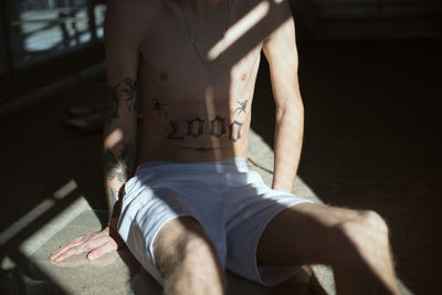 Midsection of shirtless young man with tattoo sitting on floor