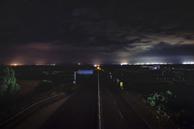 Road by illuminated city against sky at night