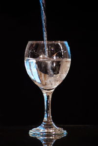 Close-up of wineglass on glass against black background