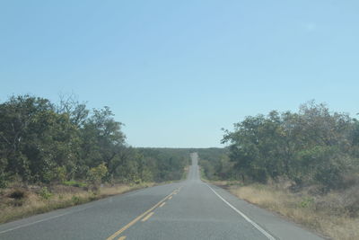 Empty road amidst trees against clear sky