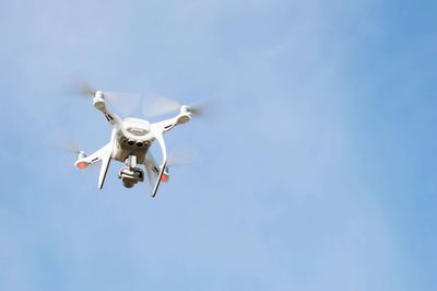 Low angle view of drone flying against clear blue sky