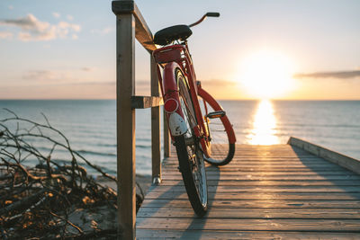 Bicycle on beach against sky during sunset