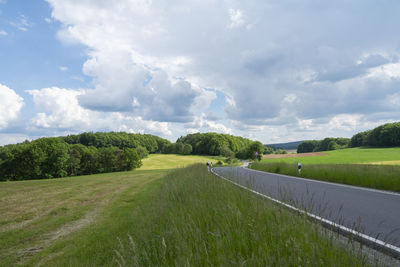 Empty road amidst field against sky