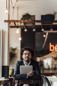 Male professional holding laptop while sitting on chair in cafe