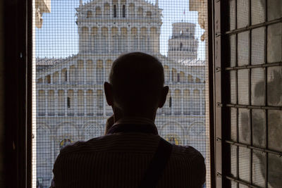 Rear view of man looking through window in building