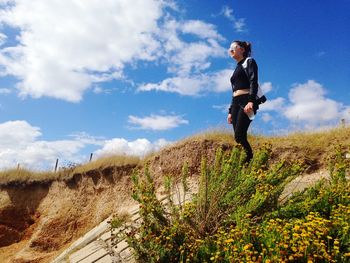 Low angle view of young woman standing on hill against sky