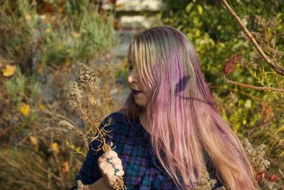 Woman with dyed hair holding plant while standing in park