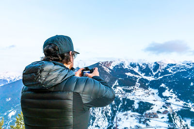 Man photographing snowcapped mountains against sky