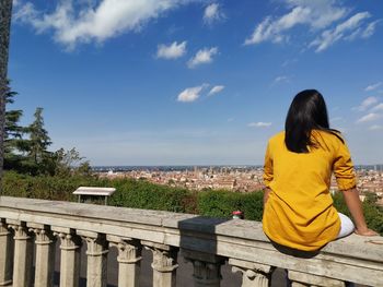 Rear view of woman sitting by plants against sky