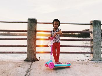 Portrait of cute girl standing on railing against sky