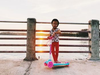 Portrait of cute girl riding push scooter on footbridge