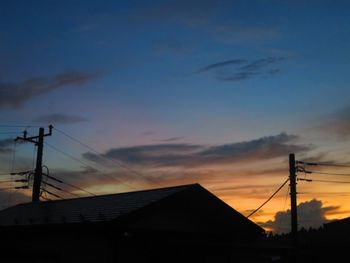 Silhouette electricity pylon and buildings against sky during sunset