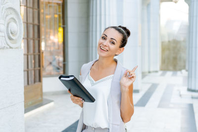 Confident young woman laughing and carrying notepad in hand while standing