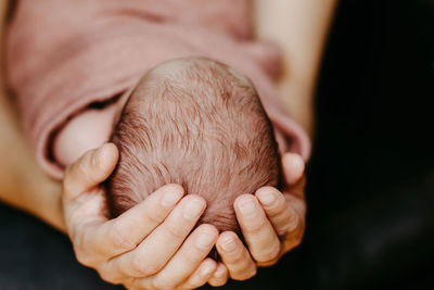 Cropped hand of mother holding newborn baby against black background