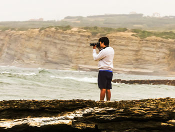 Full length of man photographing on rock at beach