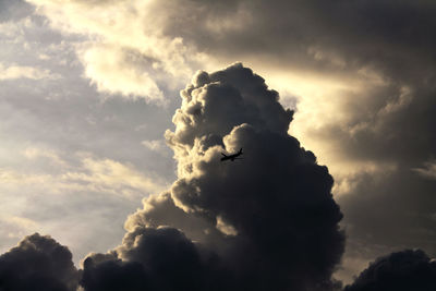 Low angle view of silhouette airplane flying against cloudy sky