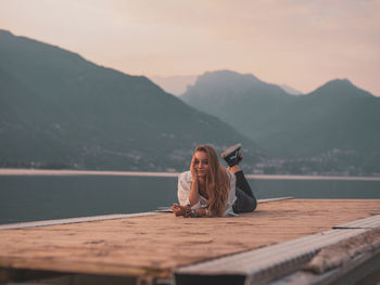 Woman sitting on wooden pier at lake against sky