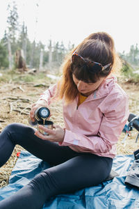 Young beautiful woman drinking hot tea or coffee from a thermos in the forest on a walk. hiking