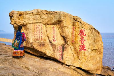 Full length of woman on rock at beach against clear sky