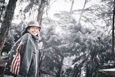 Portrait of smiling girl standing by tree in forest