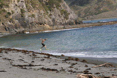 Shirtless man jumping on sea shore