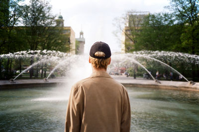 Rear view of man standing by lake against trees