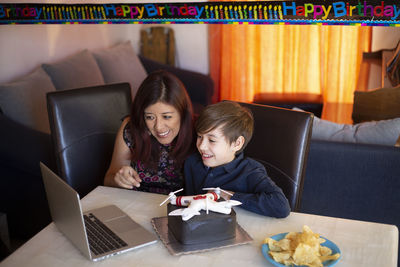 Mother with son video conferencing over laptop during birthday celebration