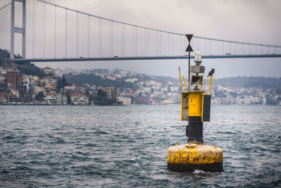 Crane on bridge over sea against sky in city