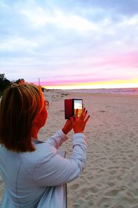 Woman photographing at beach against sky