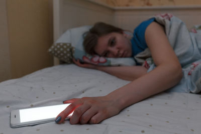 Boy using mobile phone while lying on bed at home