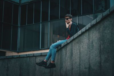 Portrait of young man sitting against wall