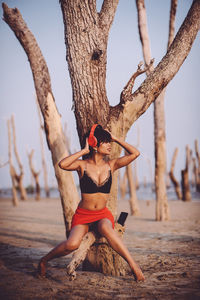 Full length of woman on tree trunk at beach against sky