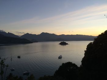 Boats sailing in sea by mountains against sky during sunset