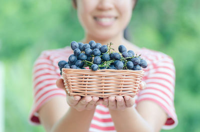 Midsection of smiling woman holding blueberries in basket outdoors