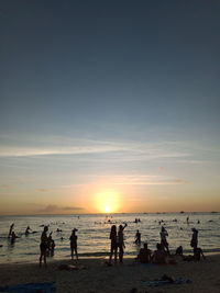 People on beach against clear sky during sunset