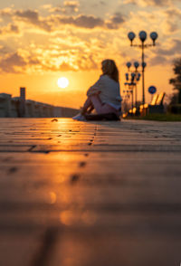 Rear view of man sitting on street at sunset