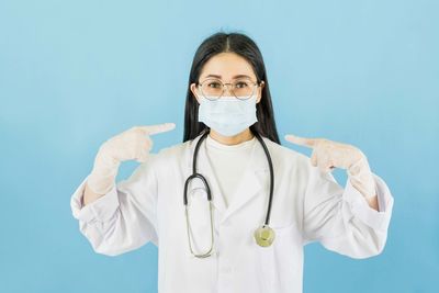 Portrait of doctor pointing while standing against blue background