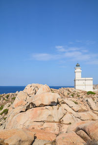 Lighthouse on rock by sea against blue sky