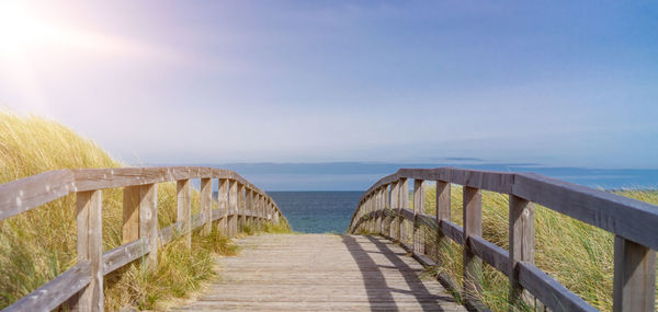 Footpath leading towards sea against sky