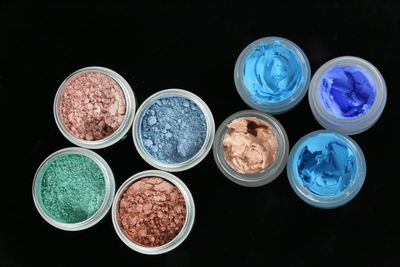 High angle view of colorful make-up product in containers on black background