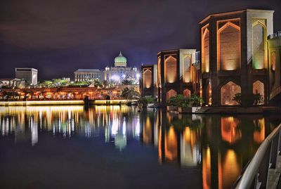 Illuminated buildings by river against sky at night